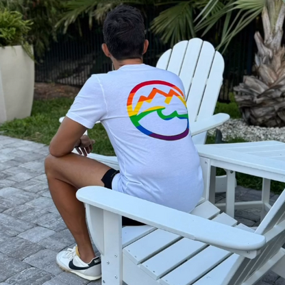 Man sitting wearing Unrefined Friends showing back of white pride shirt with rainbow logo outdoors.